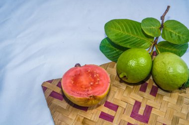 Guava izole edildi. Sarımsı yeşil derili kırmızı etli guava meyvesi koleksiyonu ve bambu hasırı ile beyaz arka planda izole edilmiş yapraklar..