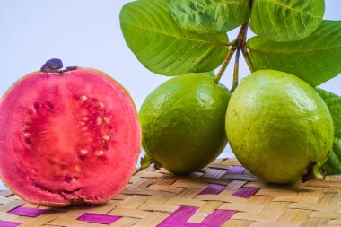 Guava izole edildi. Sarımsı yeşil derili kırmızı etli guava meyvesi koleksiyonu ve bambu hasırı ile beyaz arka planda izole edilmiş yapraklar..