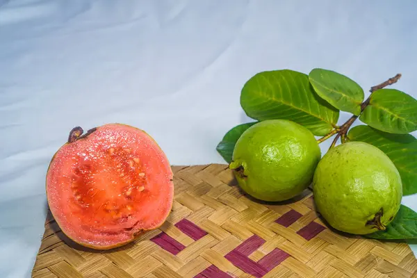 Guava isolated. Collection of red fleshed guava fruit with yellowish green skin and leaves isolated on a white background with bamboo matting.