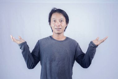 Yakışıklı Asyalı bir adamın iki elini de boş alana doğru kaldırıp iki tarafa da reklam vermesi ön planda. Reklam için izole bir arkaplan.