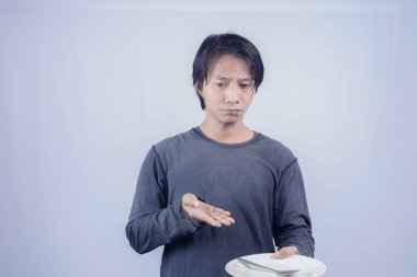 Yakışıklı Asyalı adam boş bir tabağı işaret ediyor. Kasvetli bir ifadeyle. Reklam fotokopisi için izole edilmiş beyaz bir arkaplan..