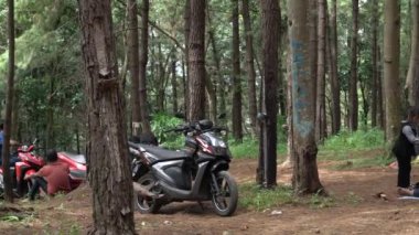 Jepara, Central Java, 17 Nisan 2024 - park halindeki motosikletli ve gölgeli ağaçlı bir kamp alanının atmosferi.