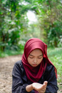 Asyalı kadın tesettürlü kayalık bir yolda kasvetli bir ifadeyle çömeliyor.