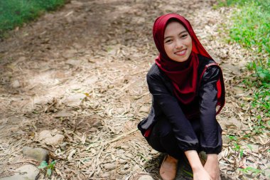 Tesettürlü Asyalı kadın, ormanda kayalık bir yolda kameraya gülümsüyor..