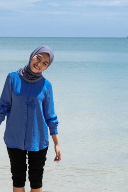 Sahilde tesettürlü Asyalı bir kadın boş reklam alanı olan parlak bir gökyüzüne karşı oynuyor..