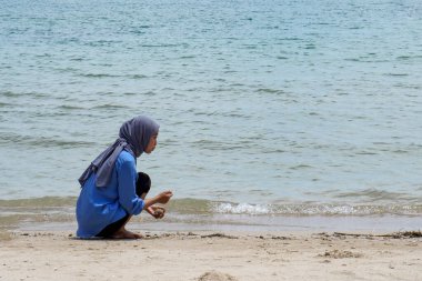 Sahilde başörtüsü takan bir kadın, deniz suyunun arka planında reklam için boş bir alanla kumsalda oynuyor..