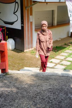 Başörtüsü takan Cava 'lı kadın parkta güneş ışığının arka planında yürüyor..