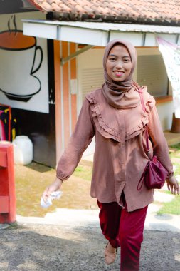 Başörtüsü takan Cava 'lı kadın parkta güneş ışığının arka planında yürüyor..