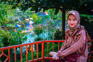 Bahçede oturan başörtüsü takan bir kadın. Fotokopi alanı olarak ağaçların arka planında oturuyor..