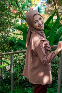 Başörtüsü takan, elleri için emniyet ütüsü tutan ve kameraya bakan bir kadının yan görüntüsü..