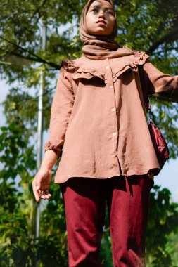 Yüzünde yaprakların gölgesi olan bir ağacın yanında peçeli bir kadın duruyordu..