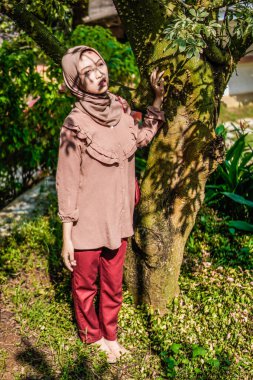 Yüzünde yaprakların gölgesi olan bir ağacın yanında peçeli bir kadın duruyordu..