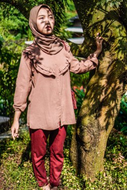 Yüzünde yaprakların gölgesi olan bir ağacın yanında peçeli bir kadın duruyordu..