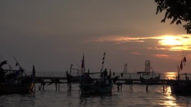 Bir grup balıkçı teknesi gece vakti turuncu gökyüzünün arka planıyla rıhtıma yanaştı..