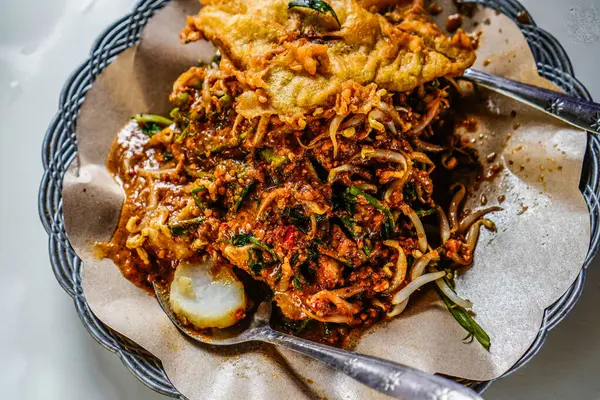 Stock image pecel dish consisting of mixed vegetables with peanut sauce and served with lontong rice, a typical Indonesian food concept.