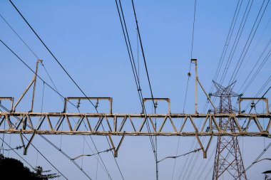 View from below of electric cables extending over train support beams on a clear sky background. clipart