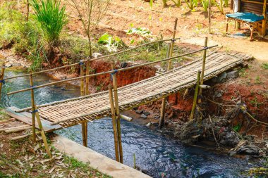 A rustic-style bamboo bridge that spans a narrow canal leading to rice fields. clipart