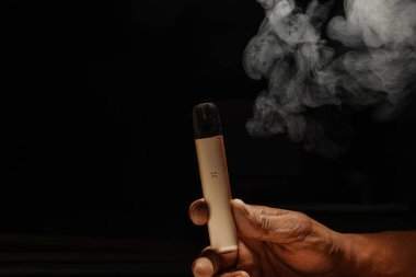 hand holding an e-cigarette on a black background with empty photocopy space. clipart