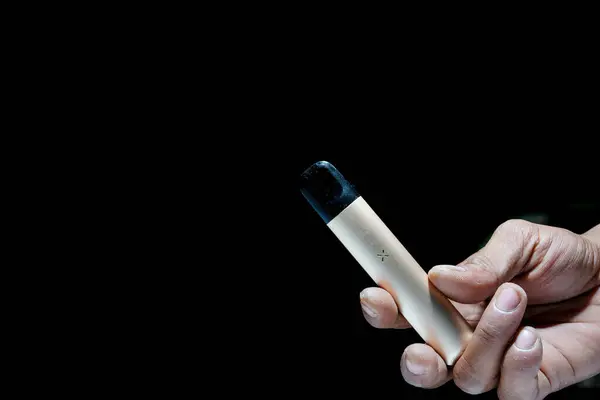 stock image hand holding an e-cigarette on a black background with empty photocopy space.