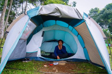 Asyalı bir adam kamp çadırında rahatça oturuyor..