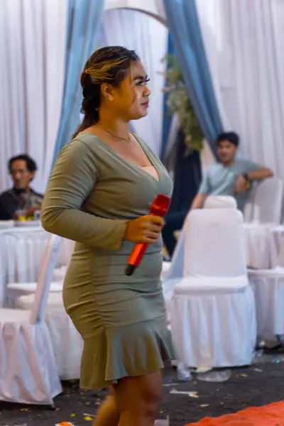 Jakarta, 2 Kasım 2024. Düğün organizasyonunda elinde mikrofonla şarkı söyleyen seksi giyinmiş kadının yan görüntüsü.,