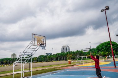 Kırmızılı adam tek başına basketbol oynuyor. Top olmadan. Topu halkanın içine atmak gibi..