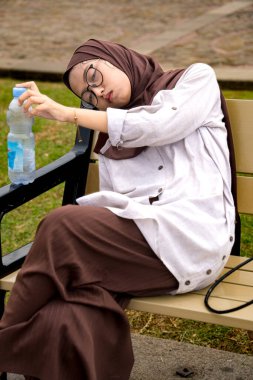 Müslüman kadınlar parktaki bankta başlarını bankın arkasına yaslayarak oturuyorlardı. Müslüman kadın yaşam tarzı kavramı. Müslüman kadın bankta uyuyor.