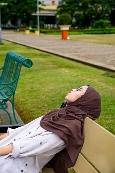 Müslüman kadınlar parktaki bankta başlarını bankın arkasına yaslayarak oturuyorlardı. Müslüman kadın yaşam tarzı kavramı. Sokakta bankta uyuyan Müslüman kadın..