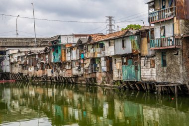 Nehir kenarındaki gecekondu evinin manzarası. Suyu kirlenmiş yeşil ve reklam odası için gökyüzü arkaplanı var. Nehrin kıyısındaki gecekondularda