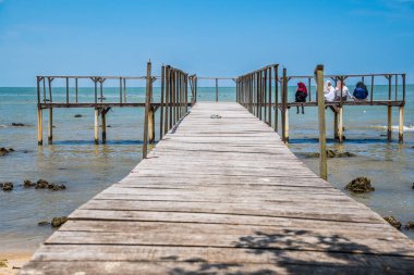 Kadınlar ahşap bir iskelede oturup etrafa bakıyorlar. Sahilin güzelliğinin tadını çıkarıyorlar. Güzel bir gökyüzü ile uzay fotokopisi çekiyorlar..