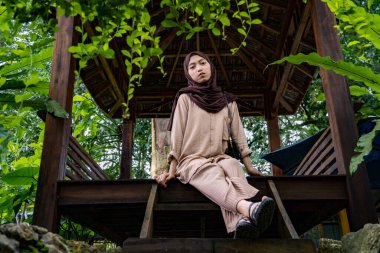 Bahçe kulübesinde oturan peçeli kadının ön görüntüsü, ahşap evde oturan güzel Asyalı kadın kameraya bakıyor.