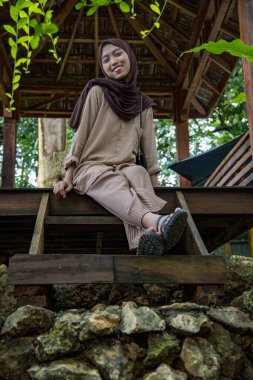 Bahçe kulübesinde oturan peçeli kadının ön görüntüsü, ahşap evde oturan güzel Asyalı kadın kameraya bakıyor.