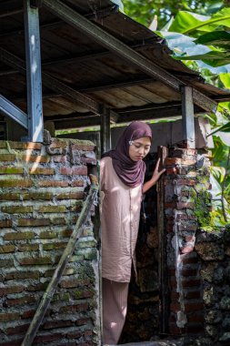 Tesettürlü Asyalı bir kadın köyde terk edilmiş eski bir evin kapısından bakıyor..