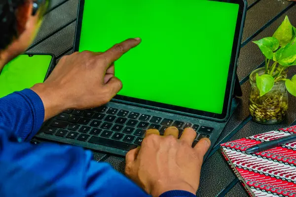 Bir adam dizüstü bilgisayarda yazıyor. Dizüstü bilgisayarı açık ve elleri klavyede. Not almak için kalemli birkaç defter var. bilgisayar ve cep telefonu ekranları reklam için boş alan