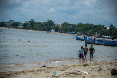 Jepara, Central Java, 30 Mart 2025, kıyıya demirlemiş balıkçı teknelerinin sesiyle sahil boyunca yürüyen çocuklar..