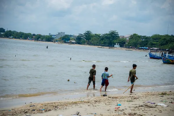 Jepara, Central Java, 30 Mart 2025, kıyıya demirlemiş balıkçı teknelerinin sesiyle sahil boyunca yürüyen çocuklar..