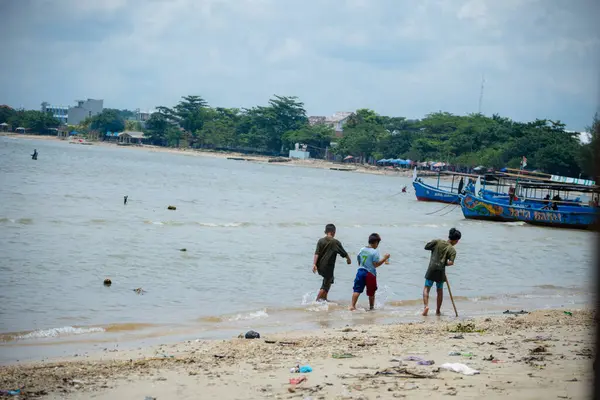 Jepara, Central Java, 30 Mart 2025, kıyıya demirlemiş balıkçı teknelerinin sesiyle sahil boyunca yürüyen çocuklar..
