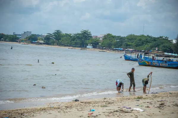 Jepara, Central Java, 30 Mart 2025, kıyıya demirlemiş balıkçı teknelerinin sesiyle sahil boyunca yürüyen çocuklar..