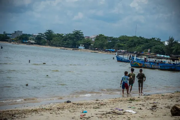 Jepara, Central Java, 30 Mart 2025, kıyıya demirlemiş balıkçı teknelerinin sesiyle sahil boyunca yürüyen çocuklar..