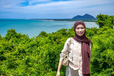 Kayalıklarda duran genç bir kadın plaj arka planında, güzel bir Asyalı kadın günlük kıyafetler giyiyor, gökyüzü ile birlikte boş bir uçurumda poz veriyor, moda fotoğrafı konsepti..