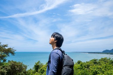 Sırt çantasıyla gezen genç adam doğanın tadını çıkarıyordu. Sırt çantalı, reklam odası için deniz ve gökyüzü olan genç bir adam..