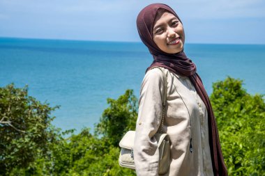 Güzel bir genç kadın, denizin kenarındaki manzaranın tadını çıkarırken gülümsedi, deniz kıyısının arka planına sahip dağın tepesinde gülümseyen güzel bir kadın..