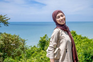 Güzel bir genç kadın, denizin kenarındaki manzaranın tadını çıkarırken gülümsedi, deniz kıyısının arka planına sahip dağın tepesinde gülümseyen güzel bir kadın..