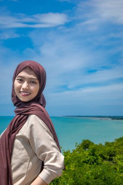 Güzel bir genç kadın, denizin kenarındaki manzaranın tadını çıkarırken gülümsedi, deniz kıyısının arka planına sahip dağın tepesinde gülümseyen güzel bir kadın..