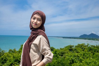 Güzel bir genç kadın, denizin kenarındaki manzaranın tadını çıkarırken gülümsedi, deniz kıyısının arka planına sahip dağın tepesinde gülümseyen güzel bir kadın..