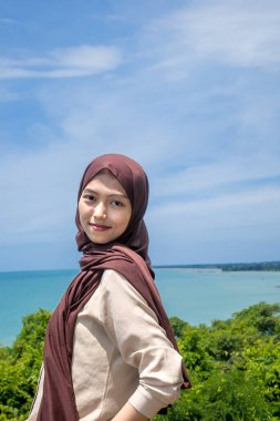 Güzel bir genç kadın, denizin kenarındaki manzaranın tadını çıkarırken gülümsedi, deniz kıyısının arka planına sahip dağın tepesinde gülümseyen güzel bir kadın..