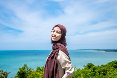 Güzel bir genç kadın, denizin kenarındaki manzaranın tadını çıkarırken gülümsedi, deniz kıyısının arka planına sahip dağın tepesinde gülümseyen güzel bir kadın..