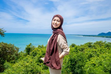 Güzel bir genç kadın, denizin kenarındaki manzaranın tadını çıkarırken gülümsedi, deniz kıyısının arka planına sahip dağın tepesinde gülümseyen güzel bir kadın..