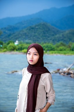 Deniz kenarında güzel bir dağ manzarası olan Asyalı Müslüman kadın, dağın arka planında kameraya bakan Müslüman kadın..