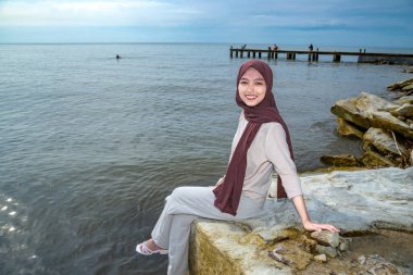 Sahilde başörtüsü ve eşarp takan güzel Asyalı genç Müslüman kadın, iskelede dinlenen Asyalı kadın, seyahat ve dinlenme konsepti..